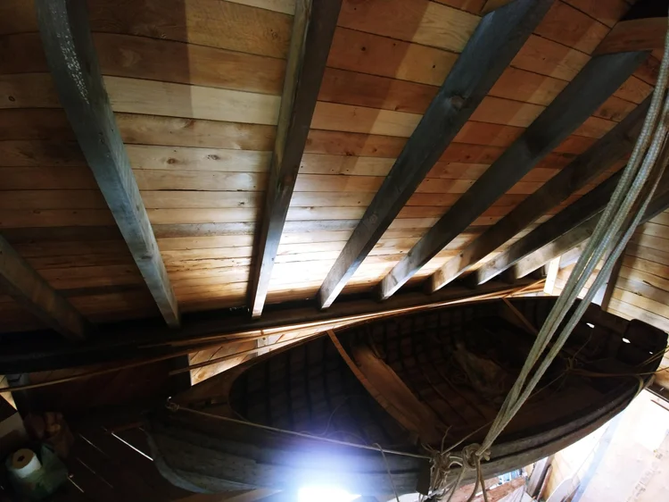 Underside view of the Ackroyd skiff hull and ribs hanging in the shop rafters
