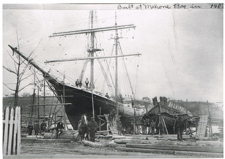 A large wooden ship 'Built at Mahone Bay in 1903' on the slipway with workers gathered around it