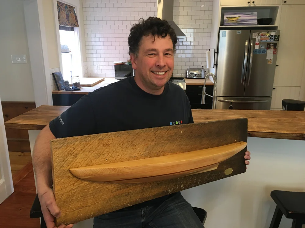 A workshop participant holding up his finished half hull model mounted on a wooden backing board