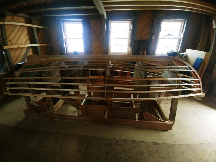 The Herreshoff dinghy tender hull frame upside-down on a strong-back inside the boatyard shed