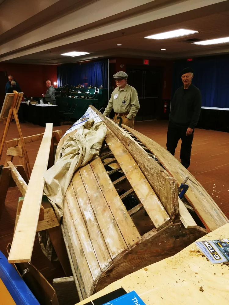 The Jolly Anne stripped of paint with two Co-op members inspecting the bare planking and frames