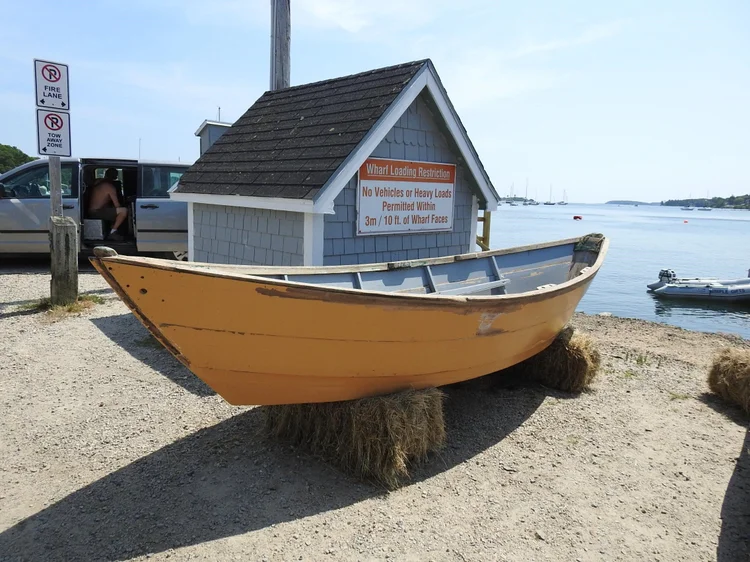 The original 1973 LaHave Dory in faded yellow paint, propped on hay bales by the wharf before restoration