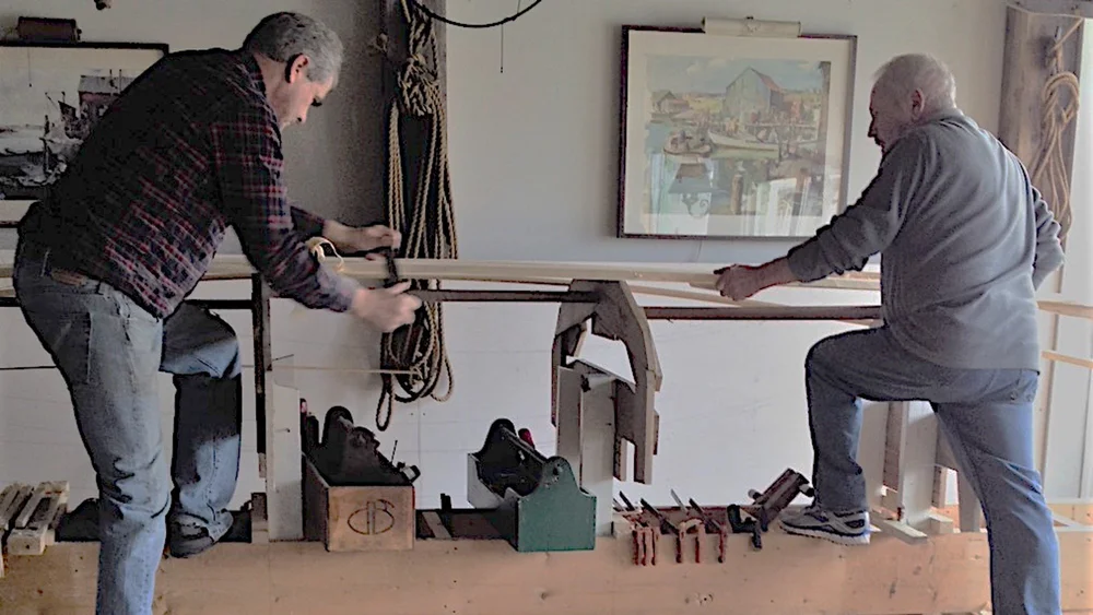 Two boatbuilders working together on a plank in the Heritage Boatyard shed