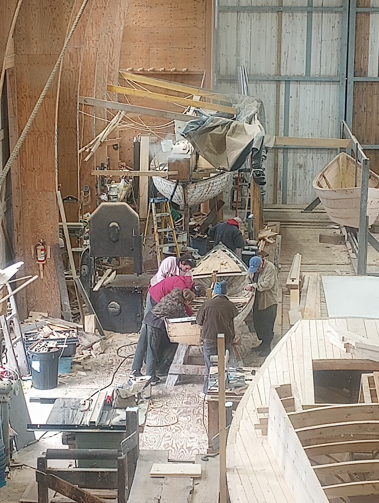 A group of volunteers shaping and fitting the Pintail Skiff inside the big shed during assembly