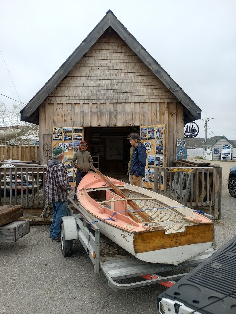 The Pintail Skiff on a trailer in front of the Heritage Boatyard shed with volunteers gathered around it