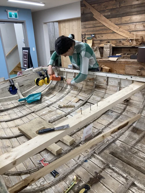 A Seraphim student drilling into a frame inside the Pintail Skiff during structural repairs