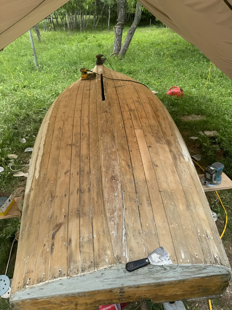 The Pintail Skiff upturned with paint stripped back to bare wood, sander and scraper sitting on the hull