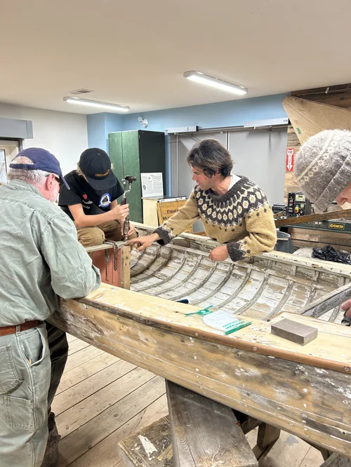 Co-op member and Seraphim students working inside the stripped Pintail Skiff hull at the boatbuilding shed