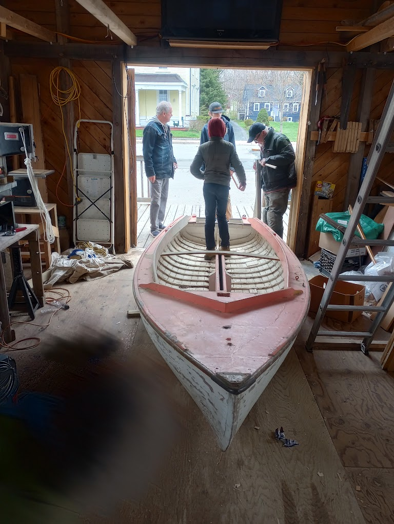 The Pintail Skiff inside the Heritage Boatyard shed with volunteers gathered around it