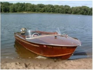 A restored Mahone Bay Plycraft 12-foot wooden runabout pulled up on a sandy shore