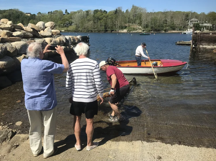 The restored Plycraft afloat at the launch ramp while David rows out and Co-op members watch from the slip