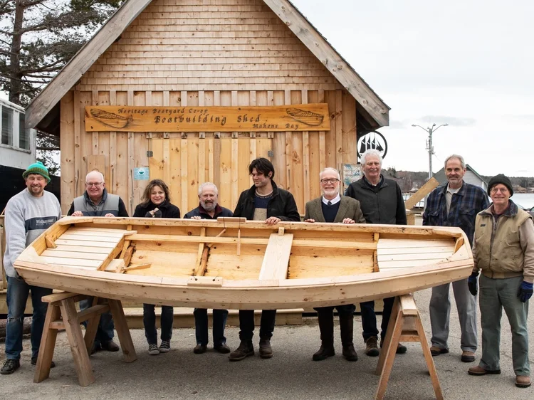 The Norwegian Pram workshop participants gathered around the finished pram in front of the Heritage Boatyard Co-op Boatbuilding Shed