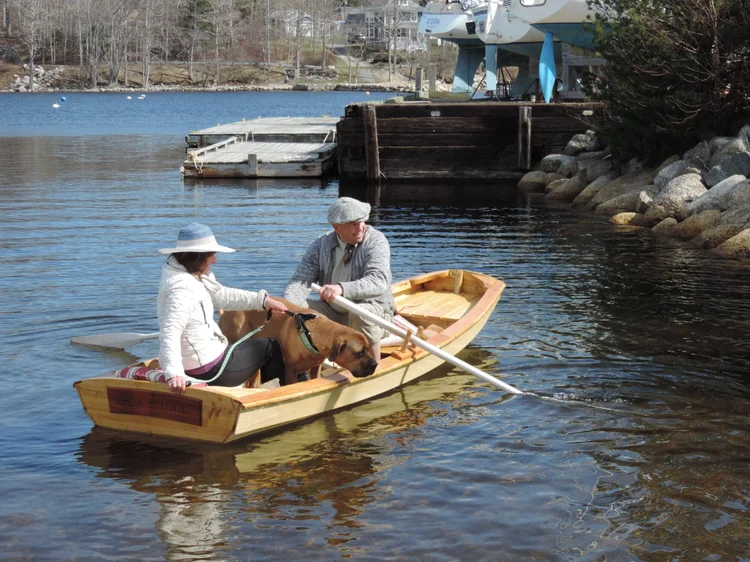 Two people and a dog rowing the finished Norwegian Pram on the water in Mahone Bay