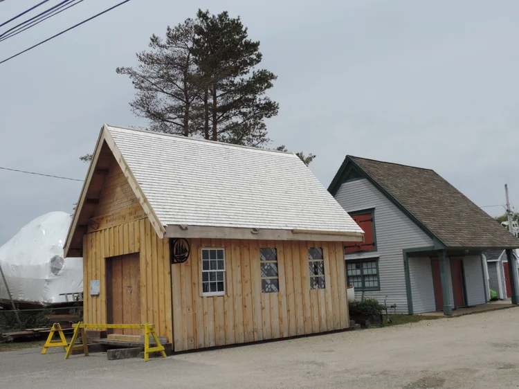 Completed boatbuilding shed clad in fresh board-and-batten siding next to the existing yard buildings