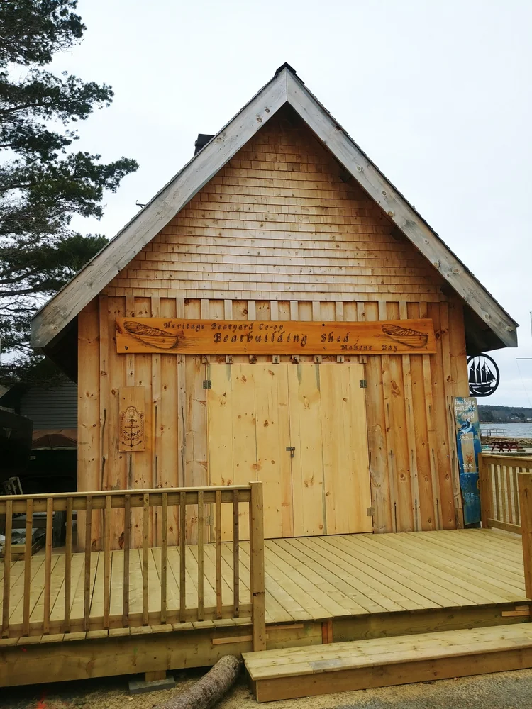 Front of the boatbuilding shed showing the carved 'Heritage Boatyard Co-op Boatbuilding Shed Mahone Bay' sign and entry deck
