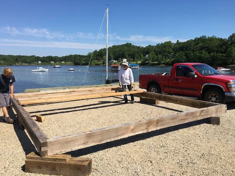 Volunteers laying out the heavy timber sill frame of the shed on the gravel pad beside Mahone Bay harbour