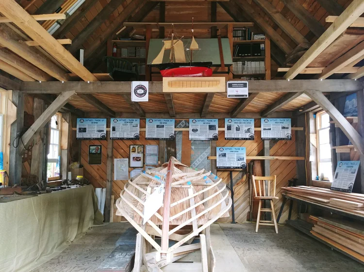 A wooden hull being built on a strong-back inside the shed