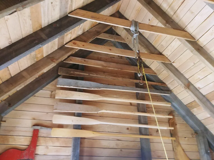 Hand-shaped wooden oars stored across the rafters inside the boatbuilding shed