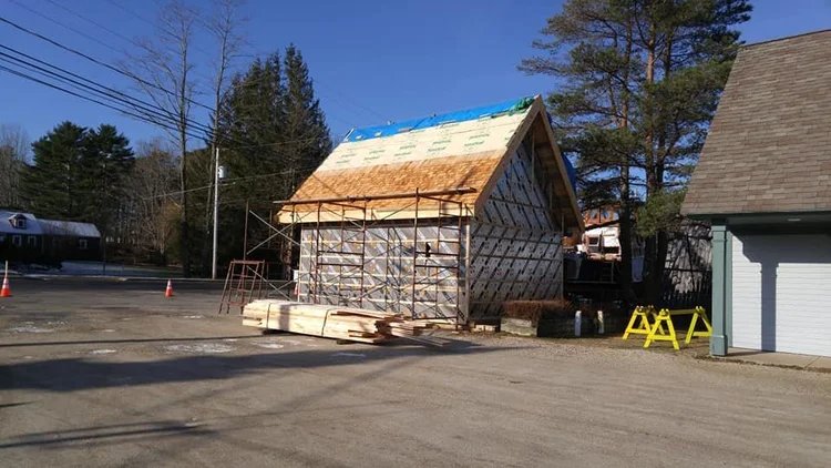 Cedar shingles being installed on the roof of the boatbuilding shed under scaffolding