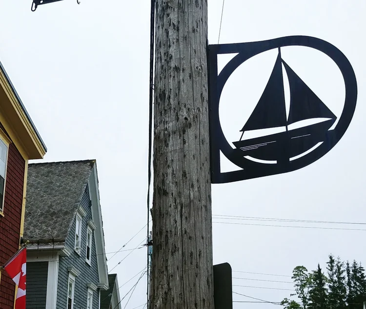 A black metal sloop silhouette sign mounted on a power pole along Main Street, Mahone Bay