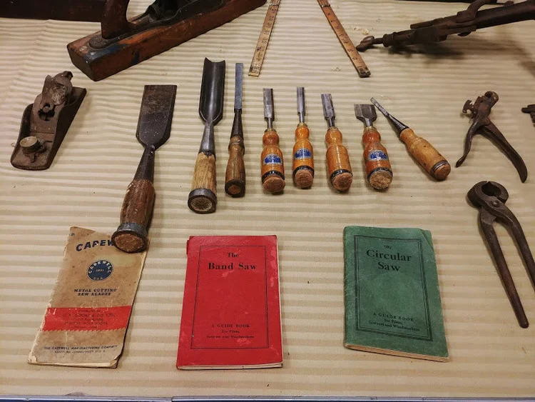 A row of antique wood chisels, planes, and vintage saw guidebooks laid out for display