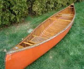 The original 1970s Tremblay canoe in faded orange before restoration, sitting on the grass